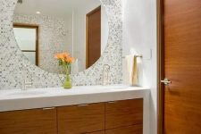 a modern elegant bathroom with an accent wall done with penny tiles, with a stained vanity, a large mirror and wall lamps