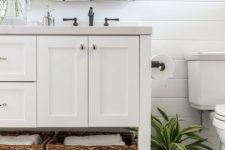 a modern farmhouse bathroom with navy walls, white paneling, a penny tile floor, a white vanity and some greenery