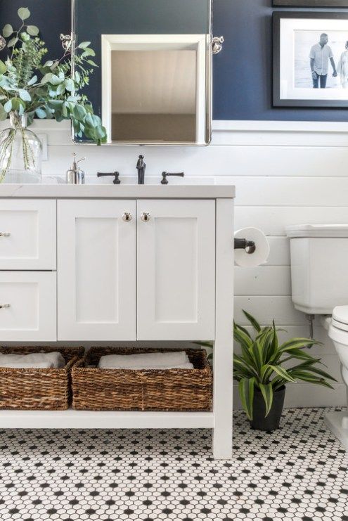 a modern farmhouse bathroom with navy walls, white paneling, a penny tile floor, a white vanity and some greenery