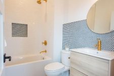 a modern neutral bathroom with white tiles, blue penny tile accents, a stained vanity, gold fixtures and a mirror