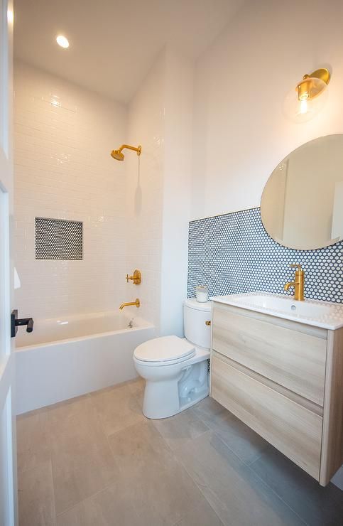 a modern neutral bathroom with white tiles, blue penny tile accents, a stained vanity, gold fixtures and a mirror