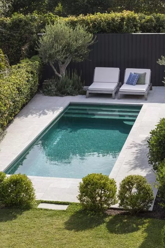 a modern outdoor space with a small pool, greenery and green lawn, white loungers and pillows is a lovely spot