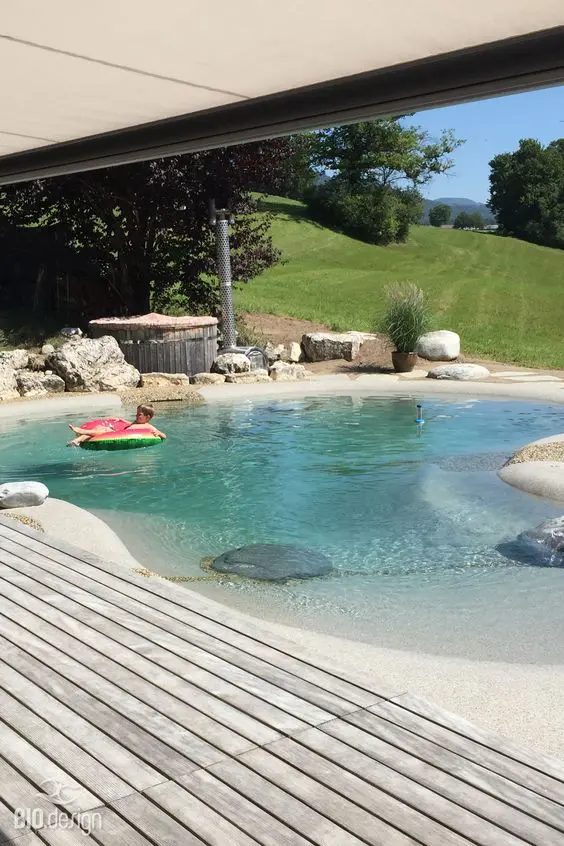 a natural looking swimming pond with rocks around and a wooden deck is a cool solution if you love natural landscaping