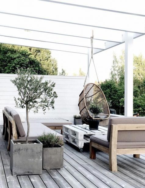 a neutral Scandinavian terrace with simple furniture, a pallet table, a rattan hanging chair and potted greenery