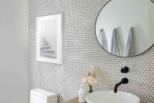 a neutral and airy bathroom clad with white penny tiles, a stained vanity, a sink, a round mirror and some art and a lamp