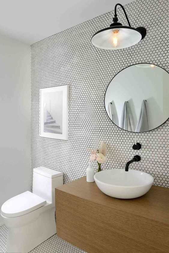 a neutral and airy bathroom clad with white penny tiles, a stained vanity, a sink, a round mirror and some art and a lamp