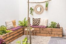 a neutral boho terrace with a large L-shaped wooden bench with greenery planted, a fire bowl and candle lanterns