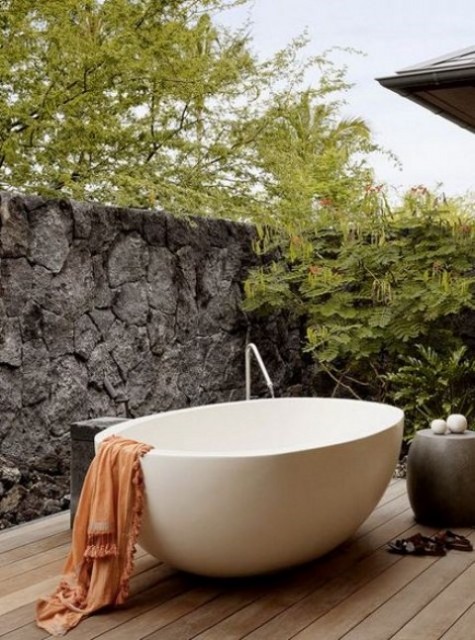 a peaceful outdoor bathroom with a stone wall for privacy, a concrete table and an oval free standing bathtub