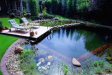 a pretty small swimming pond with a wooden border, rocks and water plants, a small deck with loungers and greenery around