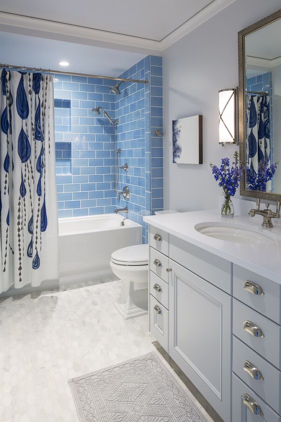 a refined bathroom in white, with blue subway tiles in the tub space, a large vanity, a printed curtain and a mirror