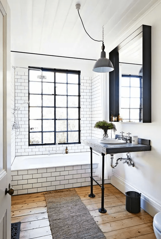 a retro industrial bathroom with the bathing zone clad with white subway tiles, a window with black frames, a mirror and a free-standing sink
