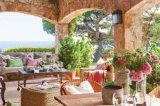 a rustic Mediterranean terrace with wicker furniture, potted greenery and blooms, wooden tables