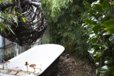 a rustic outdoor bathroom with pebbles and rocks, greenery and walls around plus a vintage tub