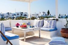 a sea Mediterranean terrace with all-wihte everything and blue and striped textiles and bold tableware