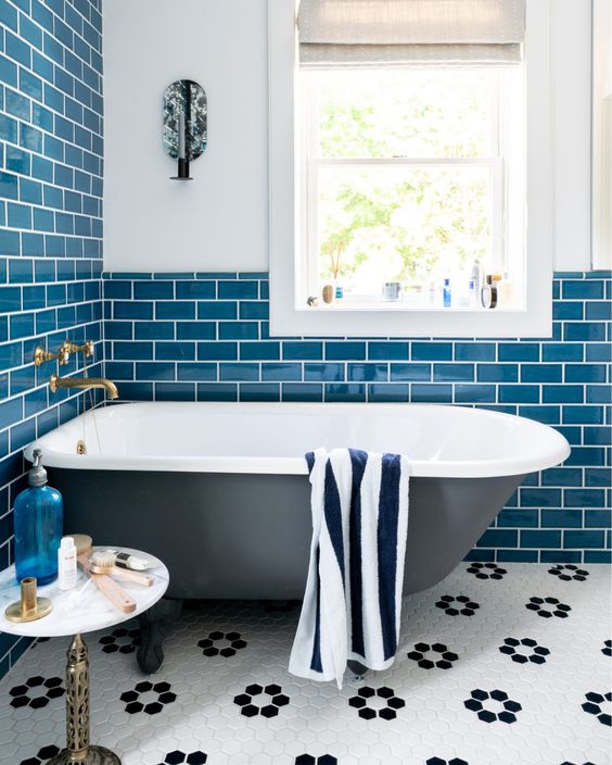 a seaside bathroom clad with blue subway tiles, a soot free-standing tub, a chic table and some decor