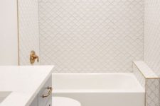 a serene bathroom clad with fish scale tiles and marble penny ones, a tub, a vanity, gold fixtures and a niche shelf