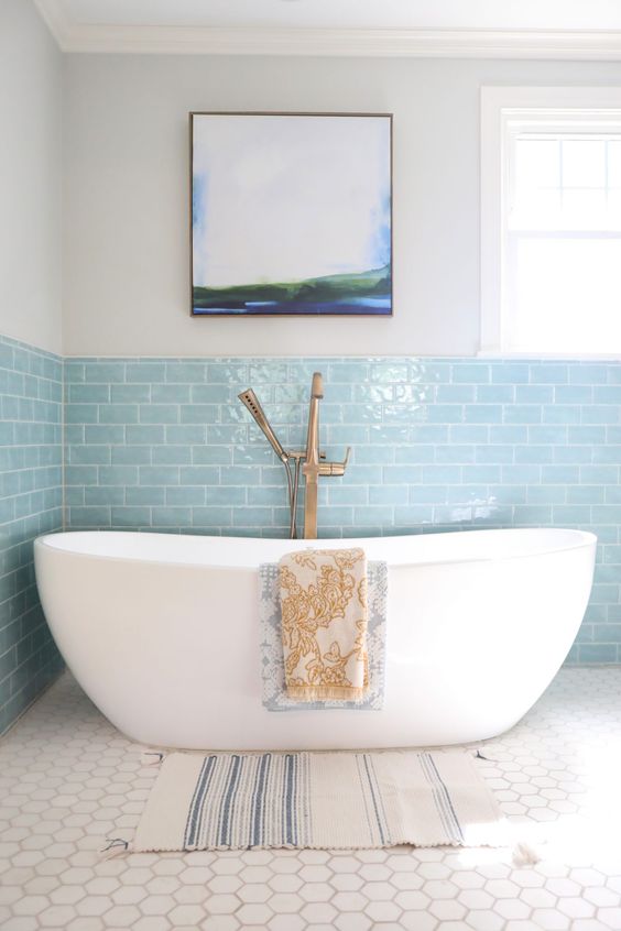 a serene coastal bathroom with light blue subway tiles and white hex ones, a tub and brass fixtures is chic and lovely