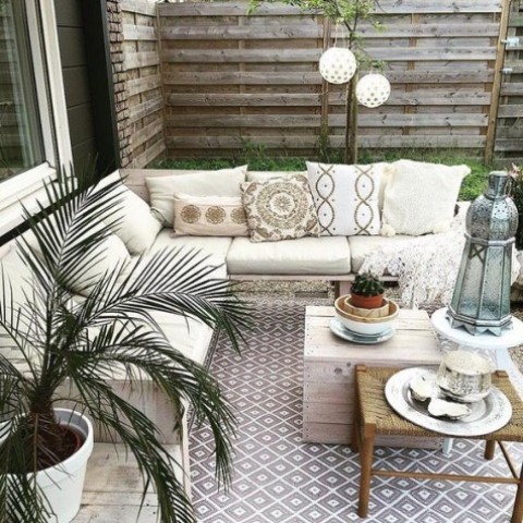 a simple neutral boho patio with printed textiles, potted greenery and wooden and wicker furniture