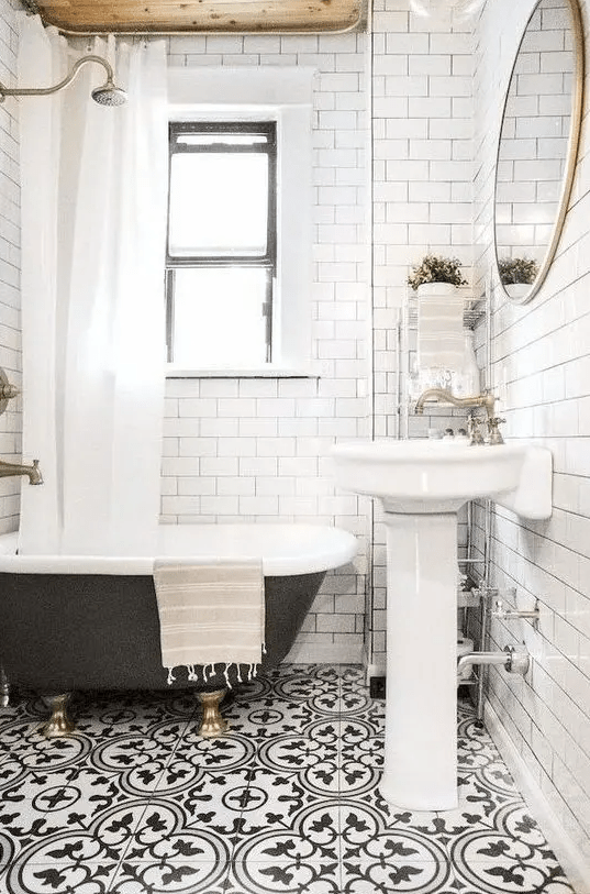 A small and bright bathroom with a mosaic floor, a wooden ceiling, a black clawfoot tub and a free standing sink
