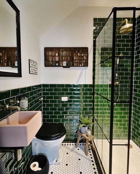 a small and bright bathroom with green subway tiles, a shower space enclosed in glass, a pink sink, a toilet and a shelf