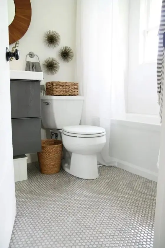 a small bathroom with a marble penny tile floor, a tub, a grey vanity, a mirror, some baskets and printed textiles