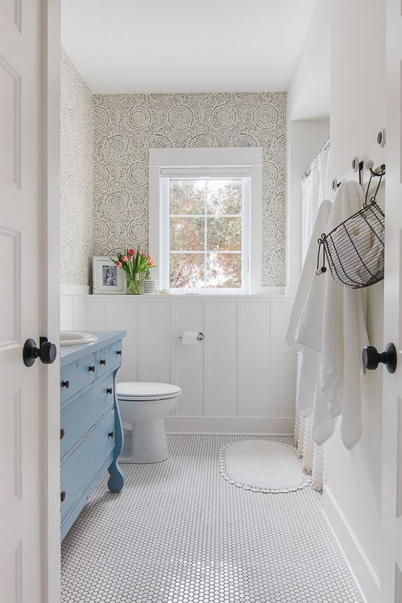 a small vintage bathroom with wallpaper, white penny tiles, a blue vaniyt, white appliances and white textiles