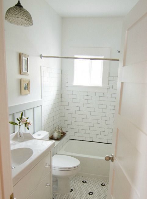 a small white bathroom clad with subway and penny tiles, a vanity, some decor and a cool pendant lamp