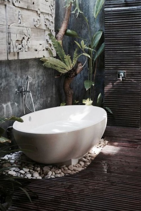 a spa-like outdoor space with a dark stained deck, cutout art on the wall, pebbles and an oval bathtub