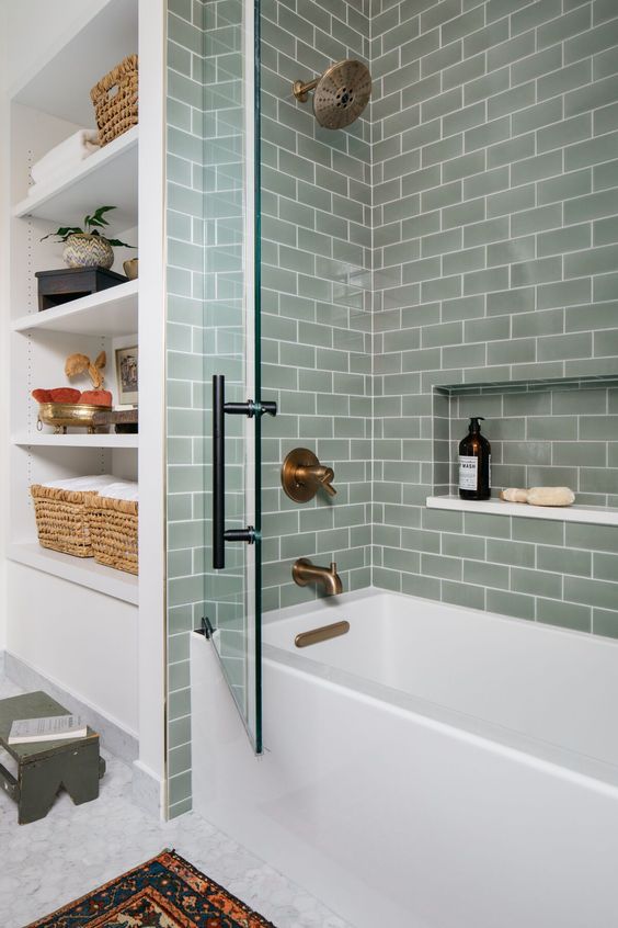 a stylish bathroom with grey subway tiles in the bathing space, a tub, built-in shelves and some lovely decor