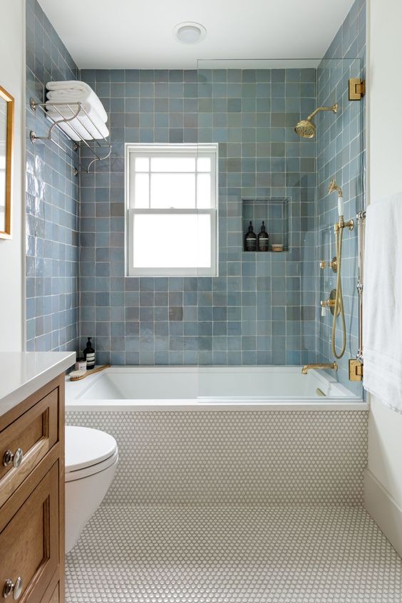 a stylish modern bathroom with blue Zellige tiles, neutral penny ones, a stained vanity, gold fixtures and white towels