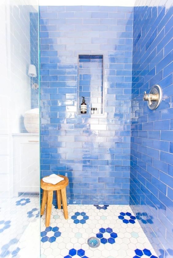a super bold shower space clad with bright blue subway tiles, a hex tile floor, a wodoen stool and a niche shelf