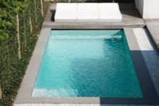 a super minimalist and stylish outdoor space with a wooden deck, gravel, a large white lounge and a plunge pool clad with tiles