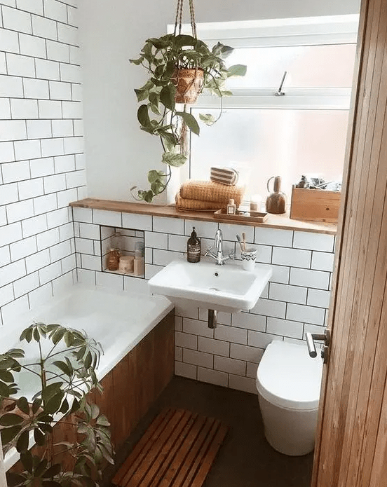 A tiny mid century modern bathroom with white subway tiles, a bathtub clad with woode, potted greenery and a window