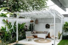 a tropical boho backyard with a plunge pool, greenery along the wall and a white cabana with some boho furniture