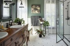a vintage bathroom with green walls, white subway and penny tiles, a vintage vanity, sinks, mirrors, lace curtains and greenery