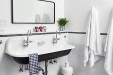 a vintage bathroom with white subway and navy penny tiles, a vintage sink, a mirror and red lamps plus textiles