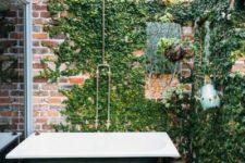 a vintage industrial outdoor bathroom with a brick wall covered with vines and a green bathtub