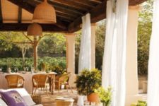 a welcoming Mediterranean terrace with wicker furniture and lampshades, potted greenery, white curtains to hide from the sun