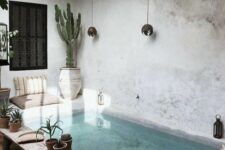 a welcoming Moroccan backyard done with concrete and tiles, Moroccan pillows, wall lamps and potted cacti