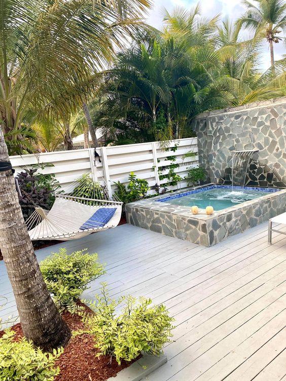 a welcoming outdoor space with a weathered wooden deck, a stone clad pool and wall, a hammock and greenery around