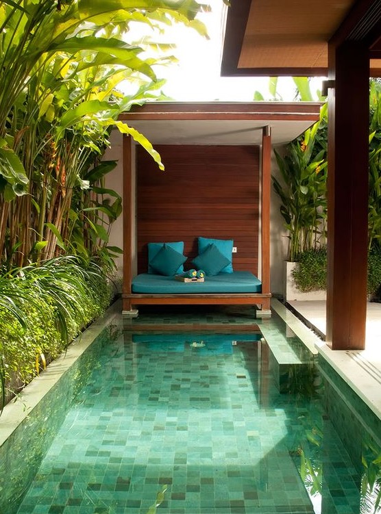 A welcoming tropical backyard with a rustic cabana, a small pool with mosaic tiles and built in benches