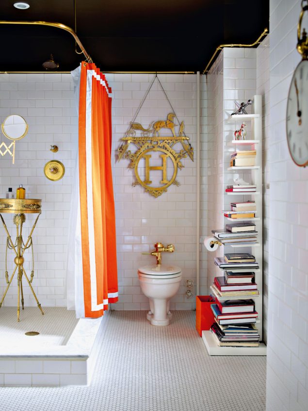 a whimsical bathroom with white subway and penny tiles on the floor, a shower with a gold stand, a gold decoration, a bookshelf and an orange curtain