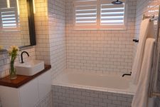 a white bathroom with a black penny tile floor, a tub, a vanity, a sink and some cool pendant lamps plus black fixtures
