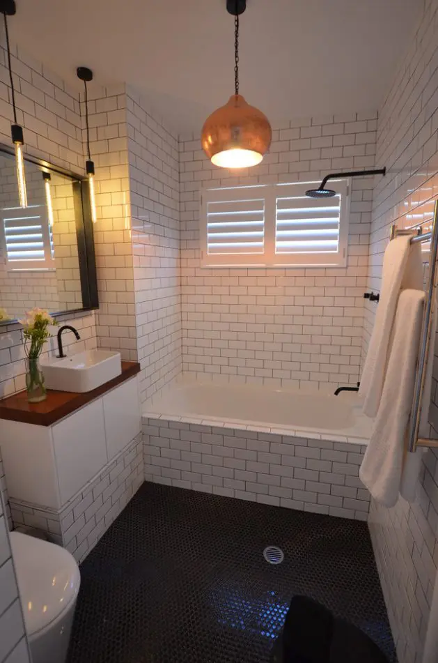 a white bathroom with a black penny tile floor, a tub, a vanity, a sink and some cool pendant lamps plus black fixtures