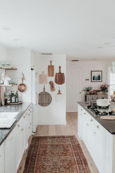 a white boho kitchen with a vintage boho rug, boards on the wall and neutral furniture with stone countertops