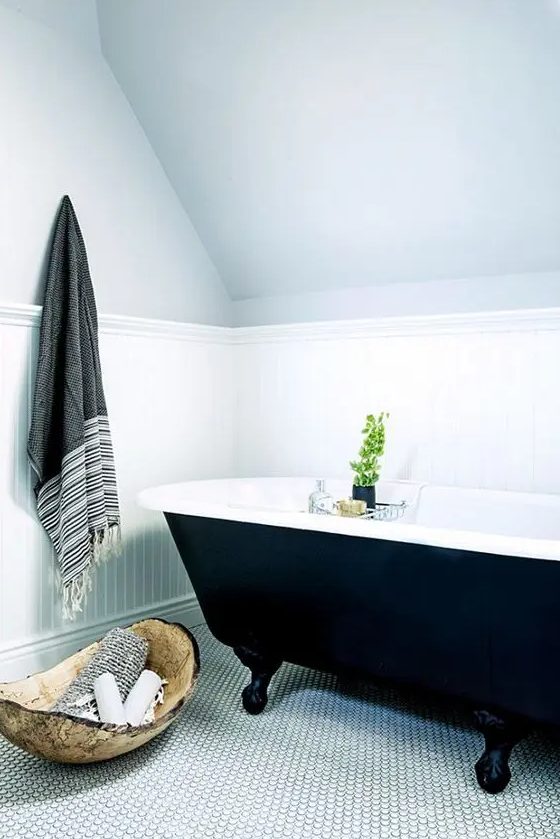 an attic bathroom with paneling, a white penny tile floor, a black free-standing tub, a bowl and some towerls