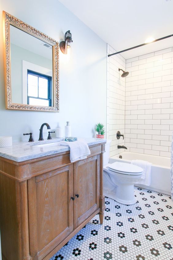 an eclectic bathroom with blue walls, white subway and black and white penny tiles, a shabby chic vanity and a mirror in a gold frame
