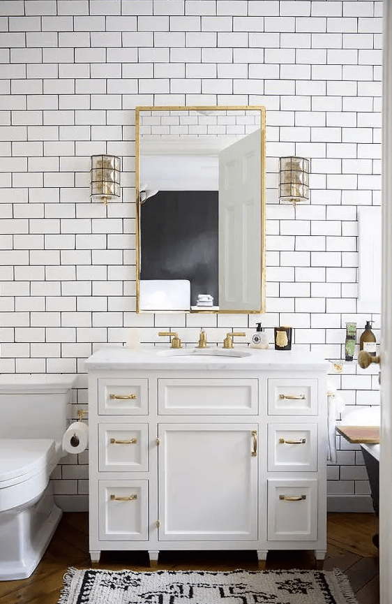 An elegant white bathroom with white subway tiles, a black free standing bathtub, gold touches and fixtures for more glam