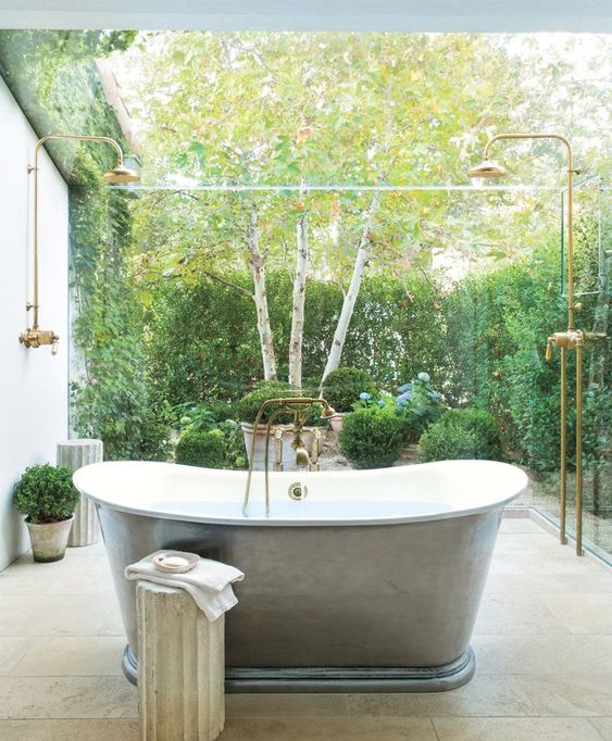 an outdoor bathroom placed in a private courtyard with greenery walls, potted greenery and a vintage tub