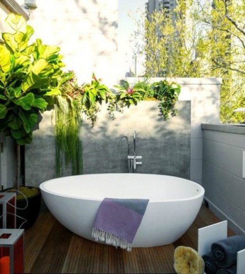 an outdoor deck with half walls all round to keep privacy yet get enough light, a stylish oval bathtub and lots of greenery
